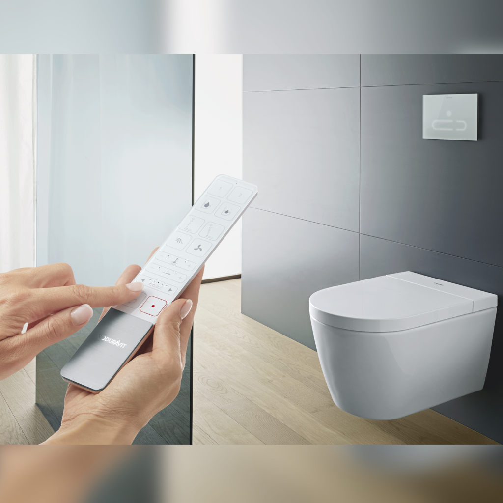 Starck f Lite SensoWash vägghängd toalett på en kaklad vägg i ett badrum. En hand som styr toaletten med en fjärrkontroll syns i förgrunden av bilen.