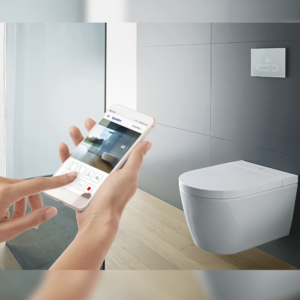 Starck f Lite SensoWash vägghängd toalett på en kaklad vägg i ett badrum. En hand som styr toaletten med en mobil syns i förgrunden av bilen.