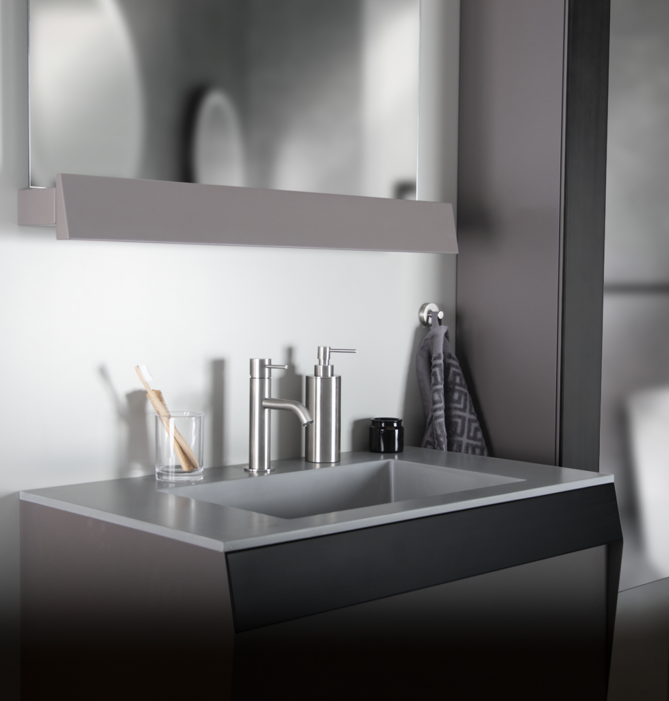 Arno rostfria tillbehör till badrum. Bilden visar en kommod med spegel, blandare och tvättställ. en tvålpump och ett glas med tandborste.