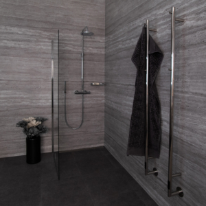 Ystad handdukstork, två stycken på en badrumsvägg. En handduk hänger på en av handdukstorkarna. Handdukstorkarna ser ut som pinnar med krokar i ovankant. I bakgrunden finns en dusch.