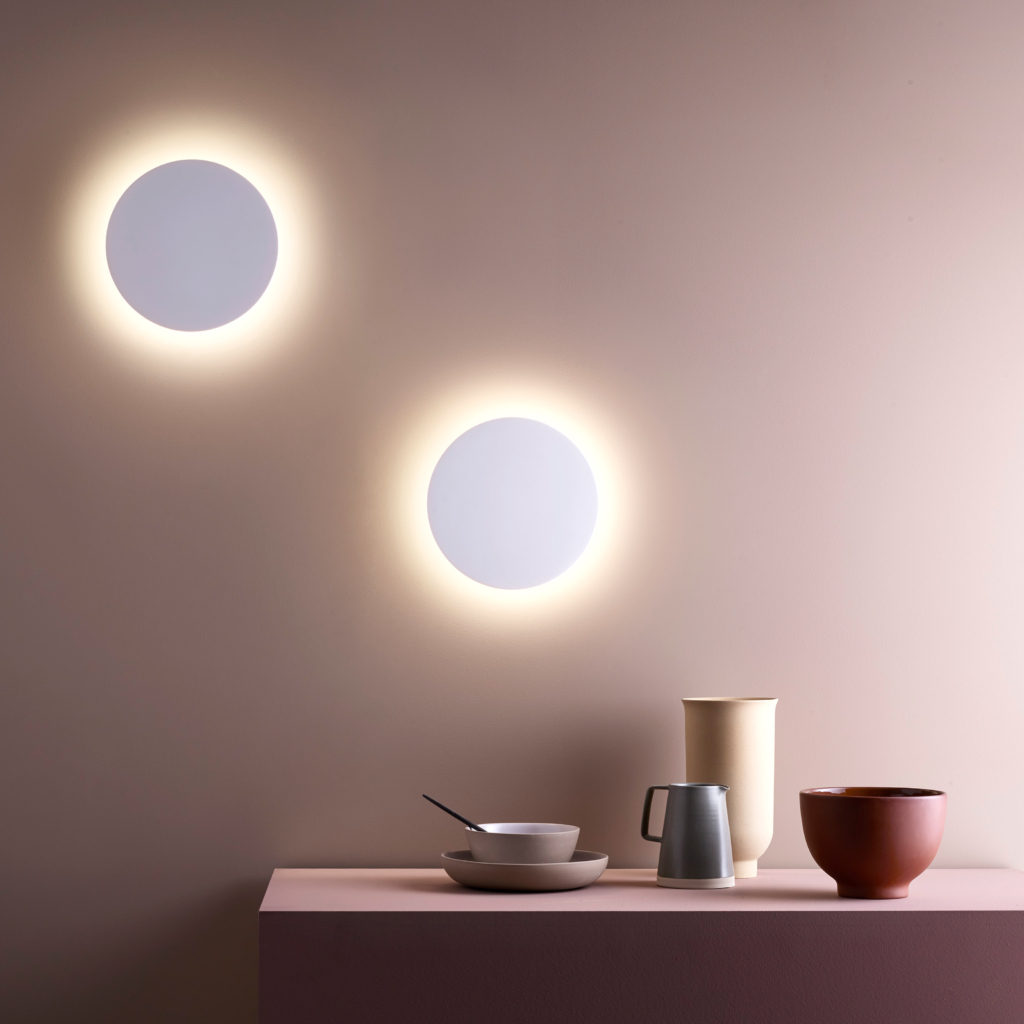 2 stycken Eclipse Round 250 LED vägglampa sitter på en vägg vid ett bord med keramik karaff och djupa tallrikar.