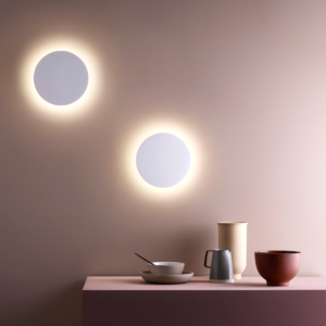 2 stycken Eclipse Round 250 LED vägglampa sitter på en vägg vid ett bord med keramik karaff och djupa tallrikar.