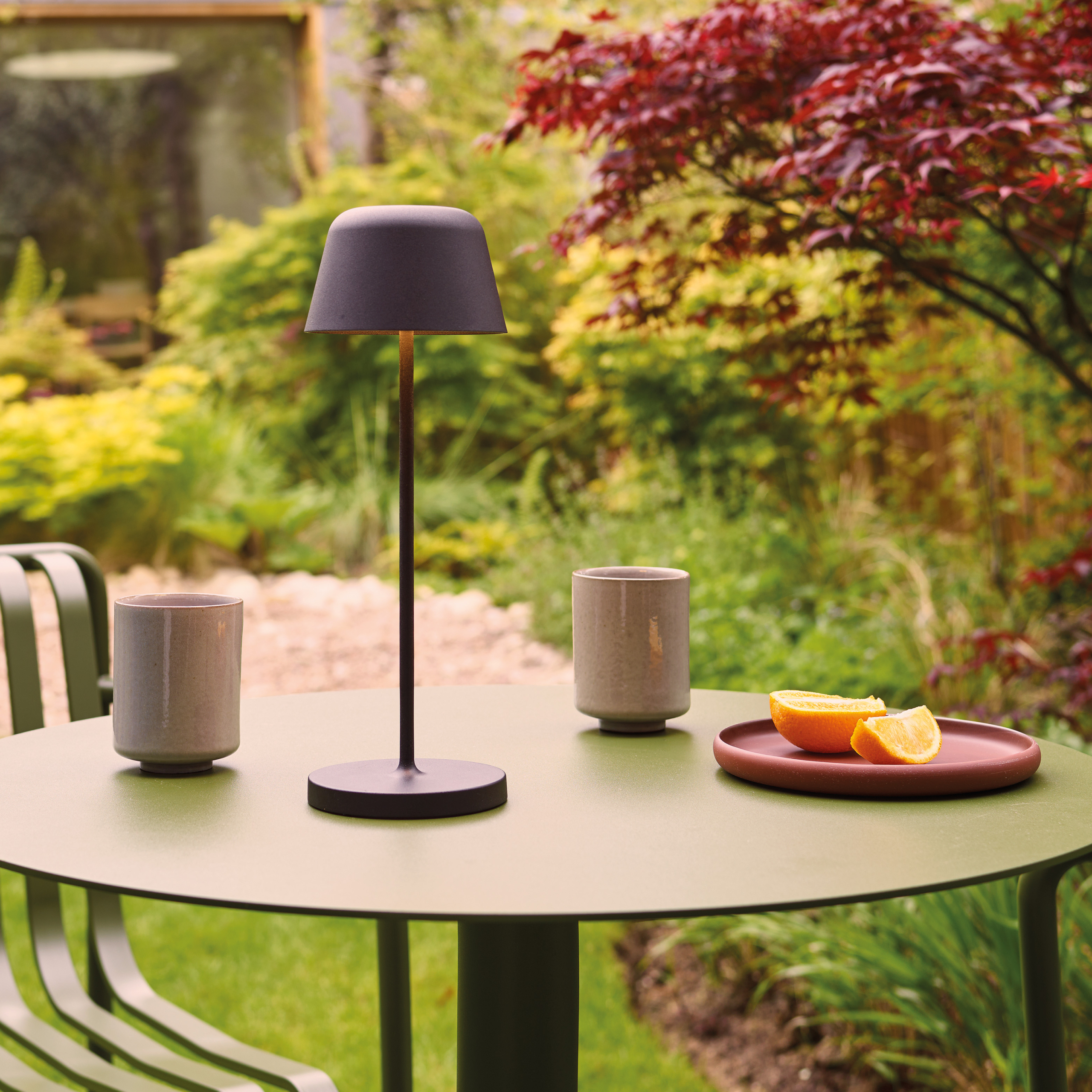 Nomad bordslampa på ett cafebord i en trädgård.
