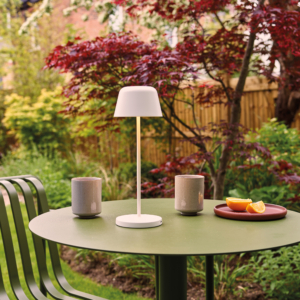 Nomad bordslampa på ett cafebord i en trädgård.