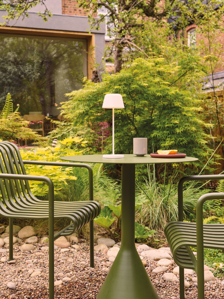 Nomad bordslampa på ett cafebord i en trädgård.